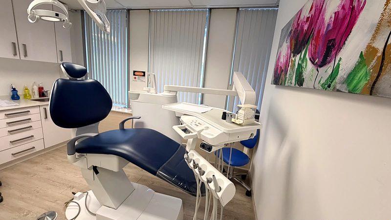 Treatment room with a navy dental chair, overhead light and delivery unit